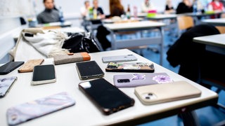 Zahlreiche Smartphones von Schülerinnen und Schülern liegen vor Beginn von schriftlichen Abiturprüfungen auf einem Tisch