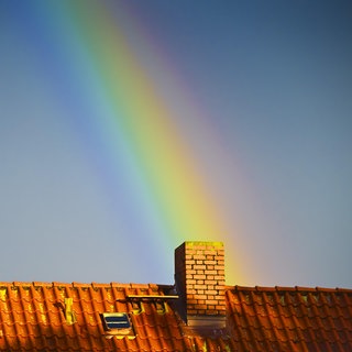 Ein Regenbogen trifft auf einem Hausdach auf einen Schornstein. Die Wärmewende betrifft viele Menschen in Baden-Württemberg. (Symbolbild)