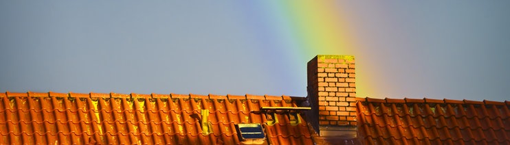 Ein Regenbogen trifft auf einem Hausdach auf einen Schornstein. Die Wärmewende betrifft viele Menschen in Baden-Württemberg. (Symbolbild)