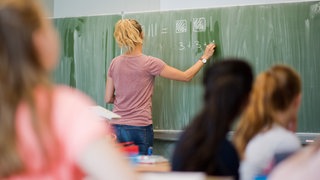 Eine junge Lehrerin schreibt im Mathematikunterricht Zahlen an eine Schultafel. Viele Lehramtsstudierende fühlen sich nicht gut auf den Beruf vorbereitet.