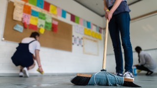 Schülerinnen und Schüler putzen ihr Klassenzimmer mit Besen und Lappen (Symbolbild).