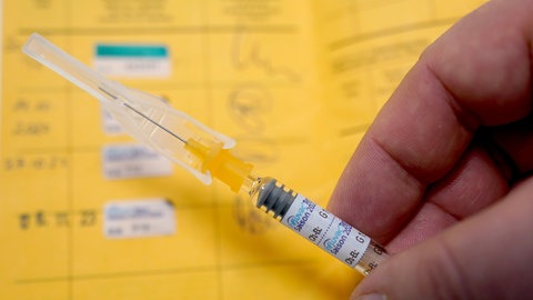 Ein Arzt hält eine Spritze mit einem Grippeschutzimpfstoff über einen Impfausweis. 