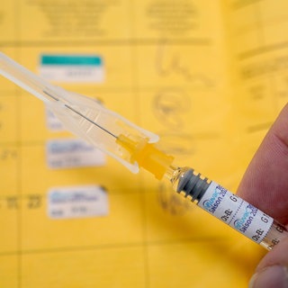 Ein Arzt hält eine Spritze mit einem Grippeschutzimpfstoff über einen Impfausweis. 