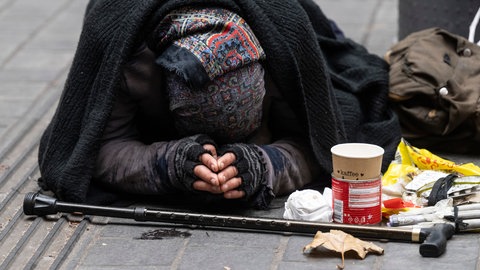 Eine Frau bettelt auf einer Einkaufsstraße um Kleingeld. 