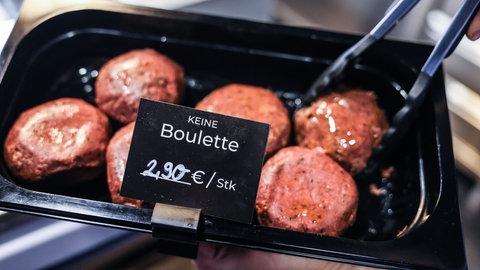 Buletten werden mit einer Zange aus der Auslage genommen. "Keine Bouletten" steht auf einem Schild vor ihnen. In einer stark kritisierten Entscheidung hat sich das Europaparlament in der vergangenen Woche für ein Verbot von Bezeichnungen wie "Tofu-Wurst" oder "Veggie-Burger" ausgesprochen. 