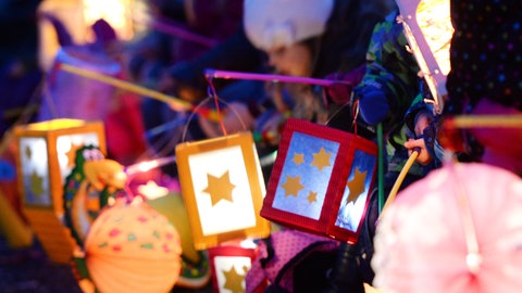 Kinder halten ihren leuchtenden, bunten Laternen in die Höhe (Symbolbild).