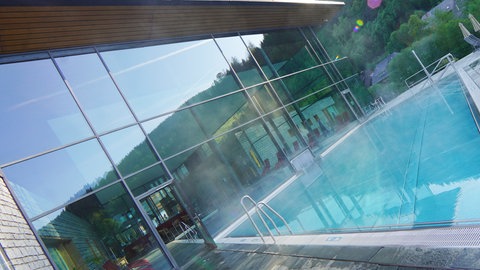 Der Außenbereich eines Schwimmbades, aus dem Becken steigt Dampf auf.