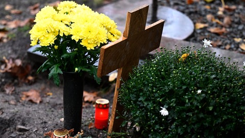 Kerzen leuchten an Allerheiligen an einem Grab. Katholiken gedenken an diesem Feiertag ihren Verstorbenen.