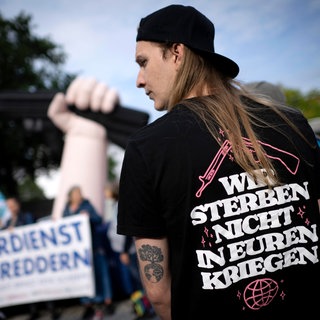  Demonstrant mit T-Shirt "Wir Sterben Nicht in Euren Kriegen" bei einer Kundgebung von Wehrdienst-Gegnern und Friedensbewegung im August 2025 vor dem Verteidigungsministerium.