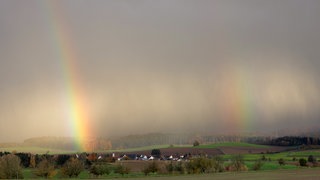 Regenbogen sind hinter einem Dorf zu sehen. Der Landtag in Stuttgart hat ein neues Grundsteuer-Gesetz beschlossen, dass Landwirten und Waldbesitzern zugute kommen soll.