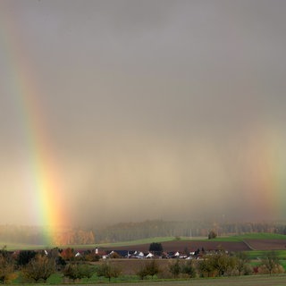 Regenbogen sind hinter einem Dorf zu sehen. Der Landtag in Stuttgart hat ein neues Grundsteuer-Gesetz beschlossen, dass Landwirten und Waldbesitzern zugute kommen soll.