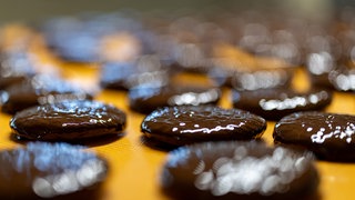 Mit einer Schokoglasur überzogen laufen frisch gebackene Lebkuchen auf einem Band in der Produktion eines Lebkuchenherstellers.