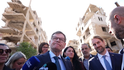 Johann Wadephul (M, CDU), Bundesminister des Auswärtigen, steht während seines Besuchs eines humanitären Projekts mit Raed Saleh (r), Minister für Katastrophenschutz in Syrien, in einer Straße vor während des Bürgerkriegs zerstörten Häusern.