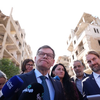 Johann Wadephul (M, CDU), Bundesminister des Auswärtigen, steht während seines Besuchs eines humanitären Projekts mit Raed Saleh (r), Minister für Katastrophenschutz in Syrien, in einer Straße vor während des Bürgerkriegs zerstörten Häusern.
