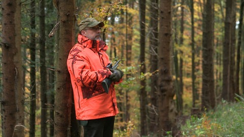 Jäger in orangefarbener Kleidung mit Gewehr bei einer Drückjagd