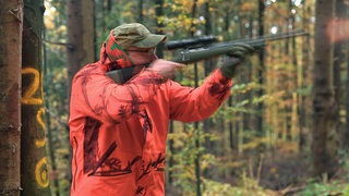 Jäger in orangefarbener Kleidung mit Gewehr bei einer Drückjagd