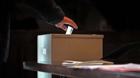 Ein Mensch wirft einen Stimmzettel in eine Wahlurne (Sujetbild)