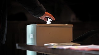 Ein Mensch wirft einen Stimmzettel in eine Wahlurne (Sujetbild)