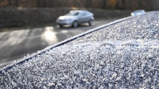 Auf einem Autodach eines Fahrzeugs, das am Rande einer befahrenen Straße steht, haben sich am Morgen bei winterlichen Temperaturen Eiskristalle gebildet. Es besteht die Gefahr von Glätte.