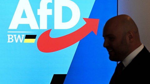 Markus Frohnmaier, Spitzenkandidat der AfD Baden-Württemberg, läuft am Logo der Partei AfD vorbei.