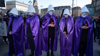 Frauen protestieren in Hamburg am Tag gegen Gewalt an Frauen für Frauenrechte und einen sicheren Zugang zu Schwangerschaftsabbrüchen. Sie tragen Kostüme, die an "The Handmaid's Tale" angelehnt sind. 