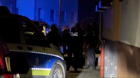 Ein Polizeiauto, mehrere Polizisten und Polizistinnen stehen vor einem Haus, sowie weitere Personen. Als ein Streit im Landkreis Karlsruhe eskalierte, wurde eine Person schwer mit einem Messer verletzt.