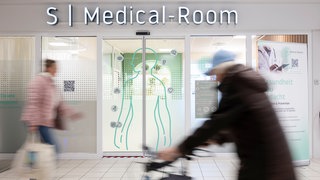 Menschen gehen in einem Kaufland-Center an einer Telemedizin-Praxis vorbei