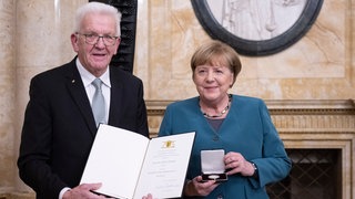 Winfried Kretschmann (Bündnis 90Die Grünen, l), Ministerpräsident von Baden-Württemberg, überreicht der ehemaligen Bundeskanzlerin Angela Merkel (CDU) im Neuen Schloss die Staufermedaille in Gold.