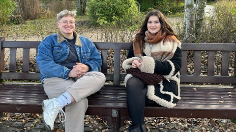 Die beiden Careleaverinnen Jamie (links) und Jette (rechts) sitzen auf einer Bank