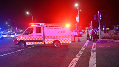 Ein Krankenwagen steht auf einer Straße, daneben Polizeibeamte, die den Tatort sichern.
