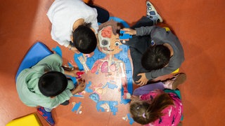 Kinder legen am Rande einer Pressekonferenz in einer Kindertagesstätte ein Puzzle zusammen.
