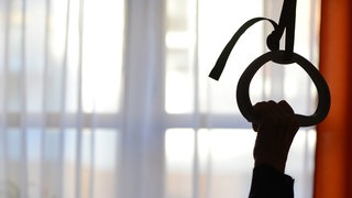 (Symbolbild) Eine Person hält sich an einer Kordel über einem Krankenbett fest. 