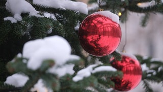 Eine rote Christbaumkugel hängt an einem Tannenbaum - bedeckt mit etwas Schnee. Gibt es Weiße Weihnachten in Baden-Württemberg? Laut SWR-Experte Michael Kost kann man das noch nicht seriös vorhersagen.