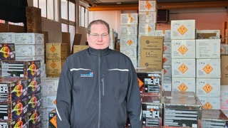 Florian Gokel ist Pyrotechniker, er steht in seinem Laden vor Packungen mit Feuerwerkskörpern.