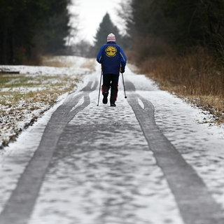 Ein Mann mit Stöcken, aber ohne Skier, ist auf der Langlaufloipe unterwegs.