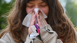 Wenn es keine Grippe oder Erkältung ist, kann es das Adenovirus sein? Eine Frau putzt sich in einem Park mit einem Taschentuch die Nase.