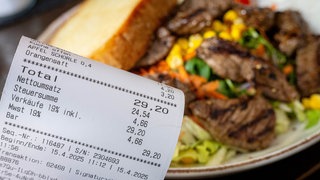 Eine Rechnung mit Mehrwertsteuer neben einem vollen Teller in einem Restaurant. 