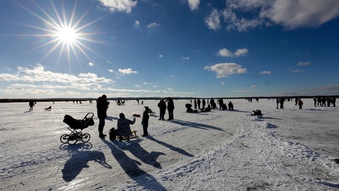 Viele Menschen befinden sich auf der Eisfläche des Federsees bei schönem Wetter