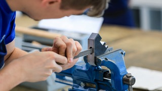 Ein Auszubildender feilt an einem Metallstück. In Baden-Württemberg gibt es immer weniger Auszubildende.