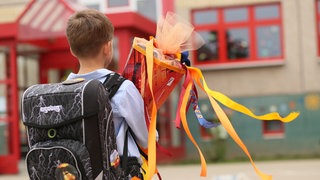 Ein Junge steht mit seiner Schultüte vor einem Schulgebäude.