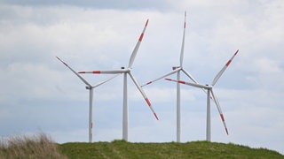 Vier Windräder hinter einem Hügel drehen sich im Wind
