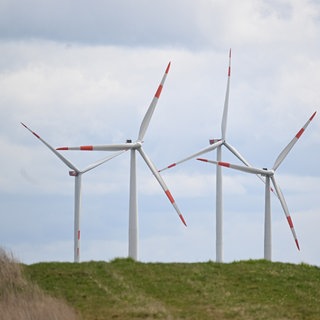 Vier Windräder hinter einem Hügel drehen sich im Wind