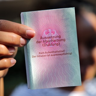 Eine junge Frau aus Afrika hält einen Ausweis für Flüchtlinge in der Hand mit dem Titel: "Aussetzung der Abschiebung (Duldung)".