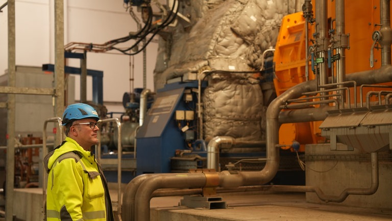 Der Geschäftsführer des Heizkraftwerks steht vor der Turbine in der aus Dampf Strom wird.