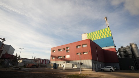 Zwei Gebäude und ein großer Schornstein im Industriegebiet in Herbrechtingen sind das Heizkraftwerk, links und rechts davon wartet Brennmaterial auf seinen Einsatz.