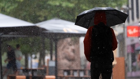 Die Silhouette eines Menschen mit Schirm, der durch den Regen geht.