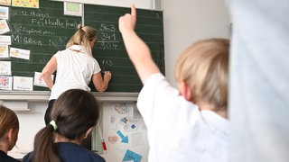 Eine Lehrerin in einer Grundschule schreibt etwas an eine Tafel