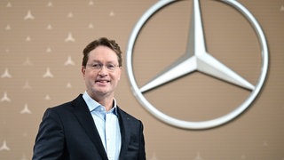 Ola Källenius, Vorstandsvorsitzender der Mercedes-Benz Group AG, steht vor der Bilanz-Pressekonferenz vor einem Mercedes-Benz Markenlogo.
