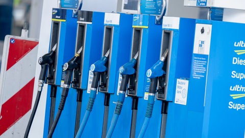 Zapfpistolen für Krafstoffe hängen in einer Haltung an einer Tankstelle. Durch den Krieg gegen den Iran sind die Spritpreise schon gestiegen. Welche anderen Auswirkungen es auf Verbraucher und Unternehmen hat.