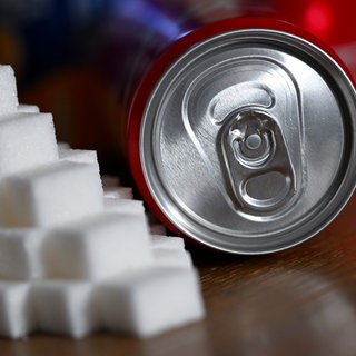 Eine Getränkedose mit einem Softdrink und zahlreiche Zuckerwürfel liegen auf einem Tisch.